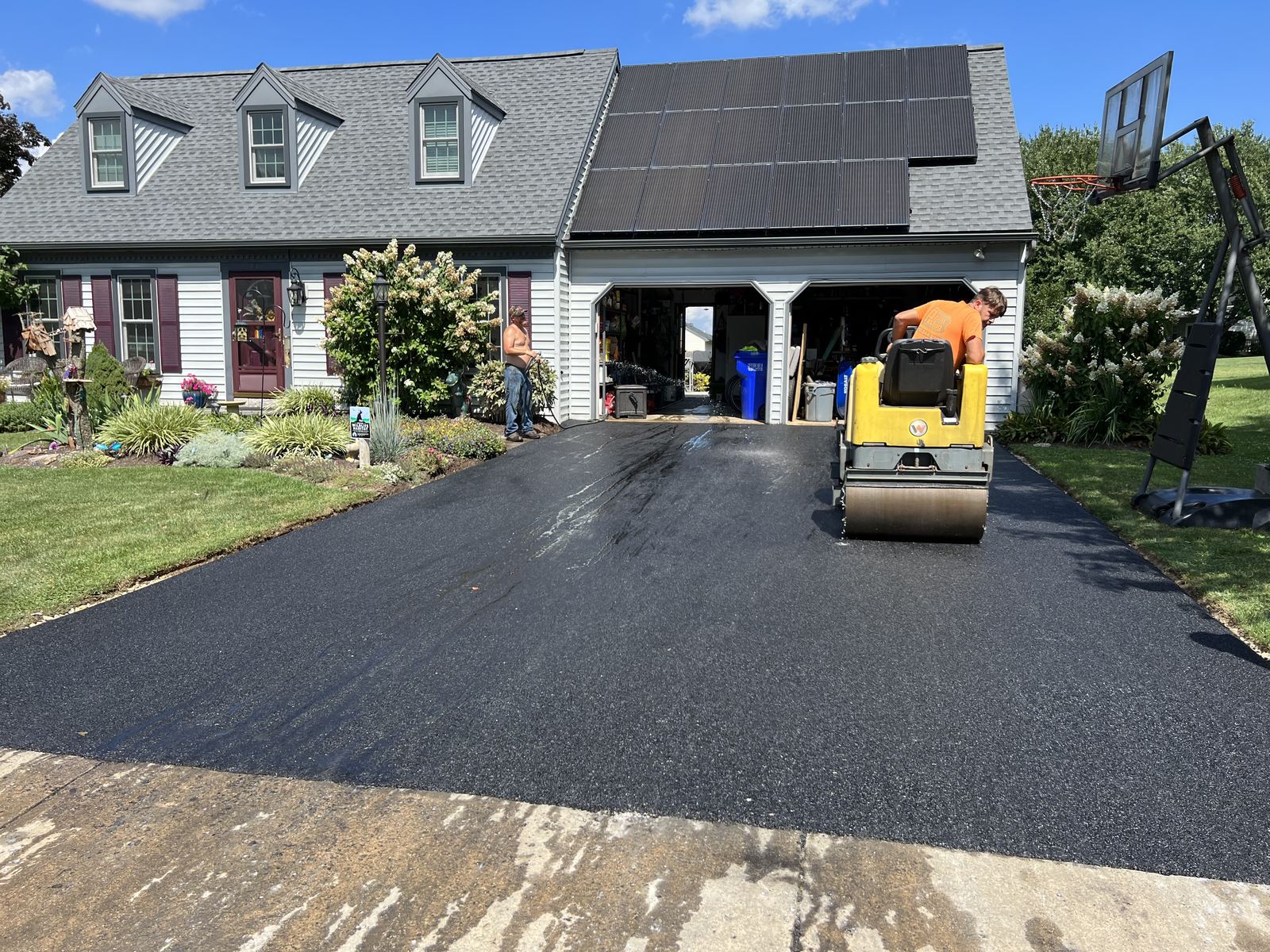 Crew rolling fresh asphalt driveway after paving